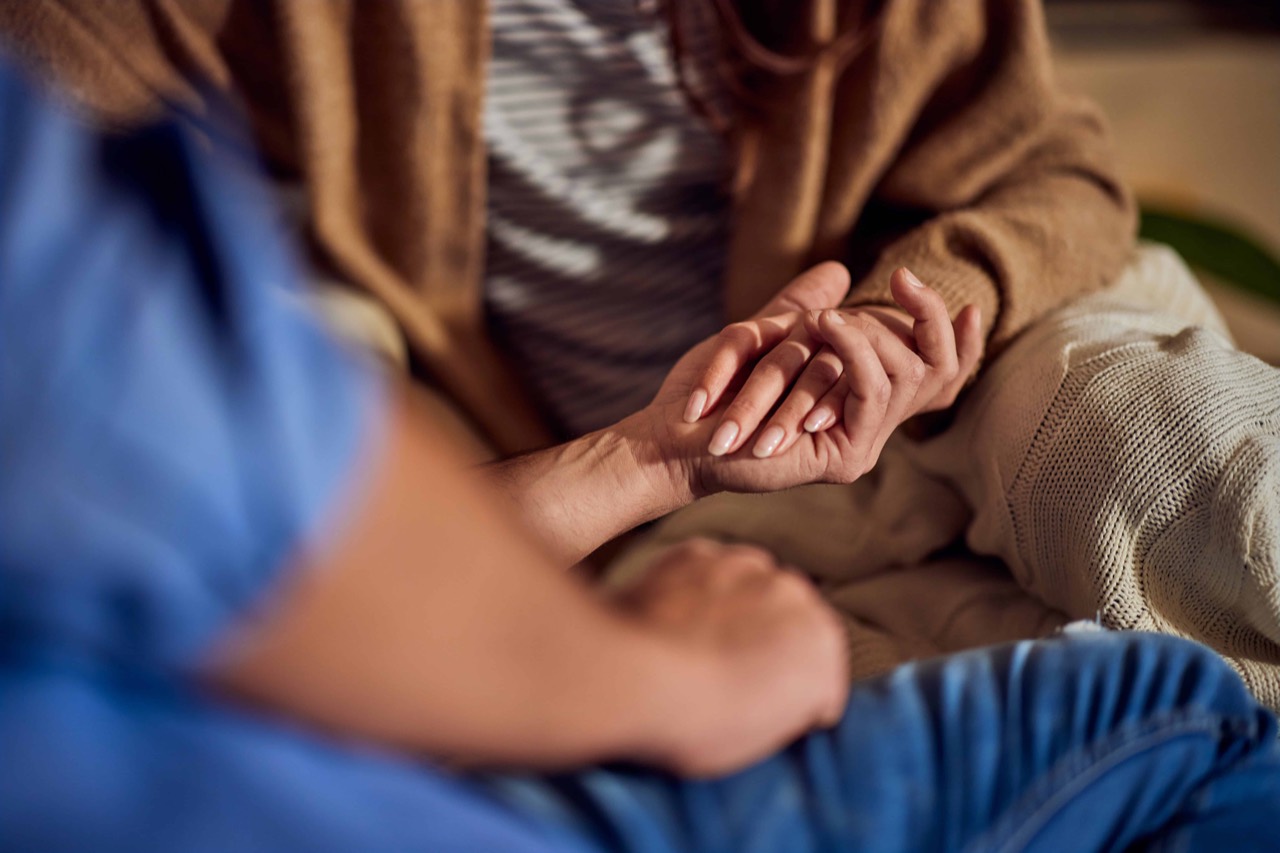 A care worker gently holding the hands of an older person